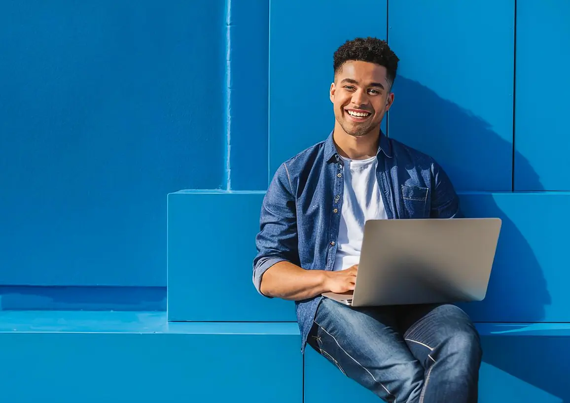 Man happily sitting on blue bench with laptop